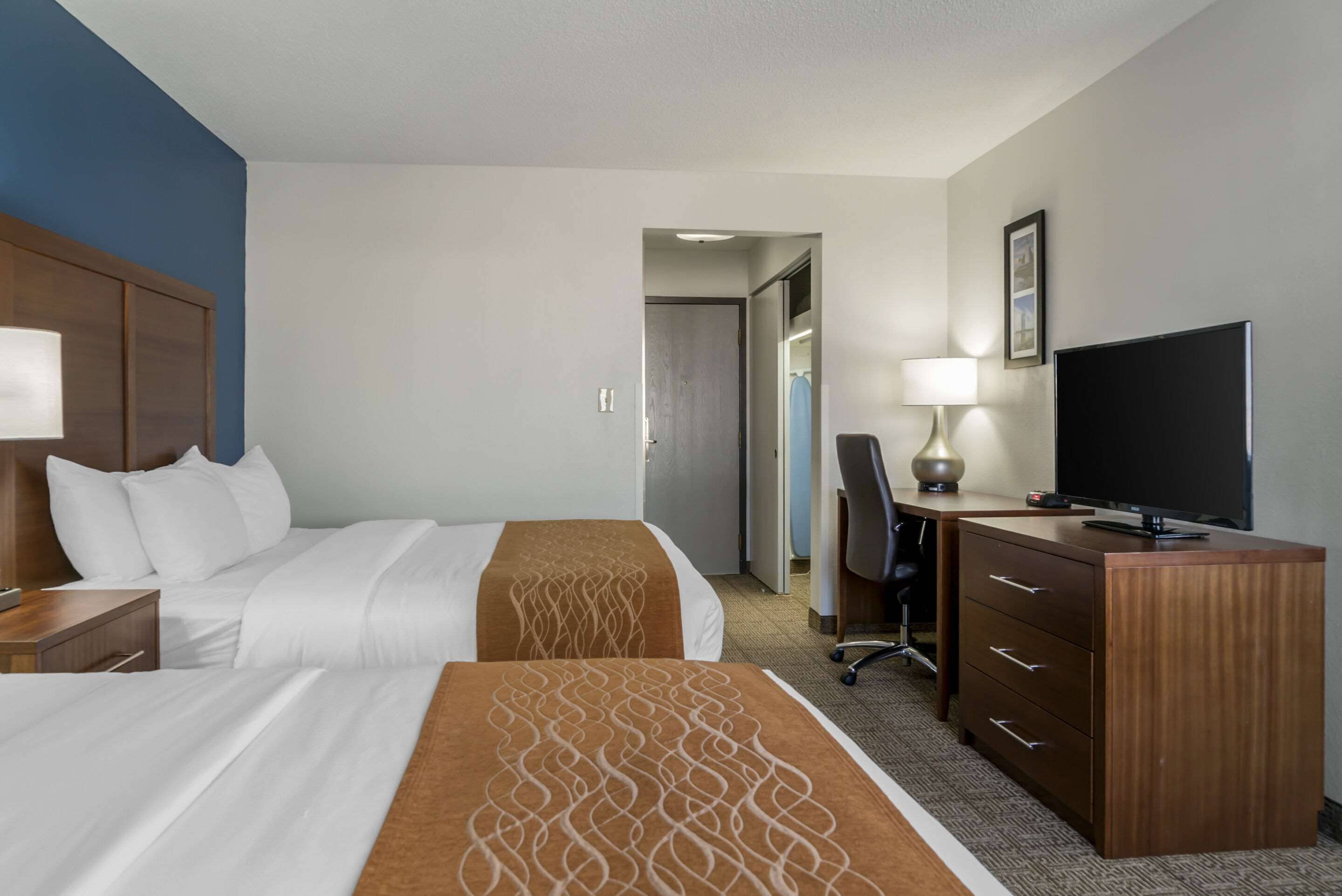 A hotel room with two beds, a desk, a television, and a lamp.