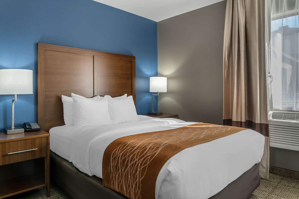 A hotel room with a large bed, two bedside tables, a nightstand, a lamp, a telephone, and a window with curtains.