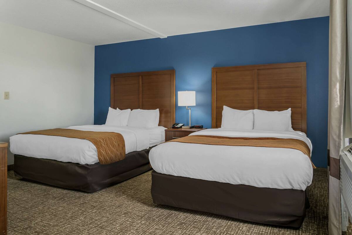 A hotel room with two beds, a nightstand, a lamp, and a window with curtains.