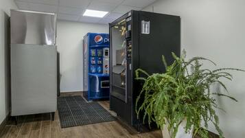 A hallway with a refrigerator, a Pepsi vending machine, and a potted plant.