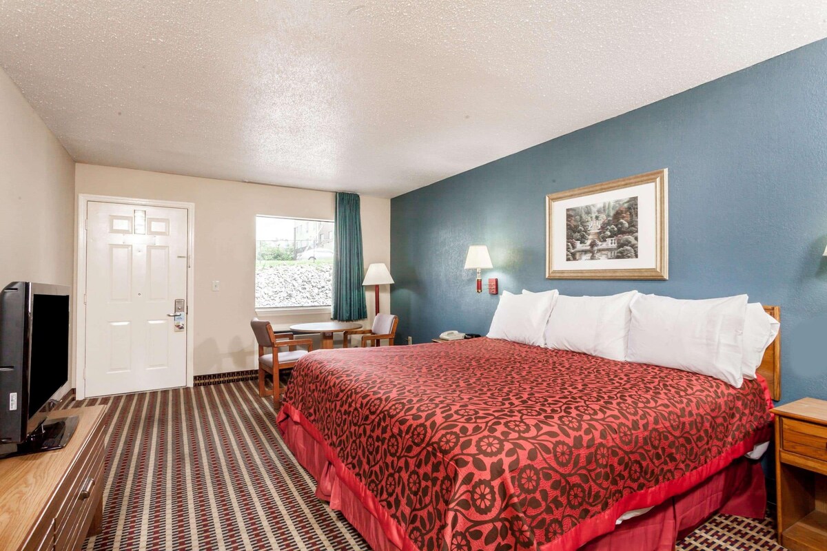 A hotel room with a bed, a desk, a chair, a television, and a framed picture on the wall.