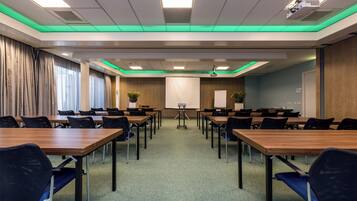 Ein Konferenzraum mit mehreren Tischen, Stühlen, einem Projektor und einer Leinwand.