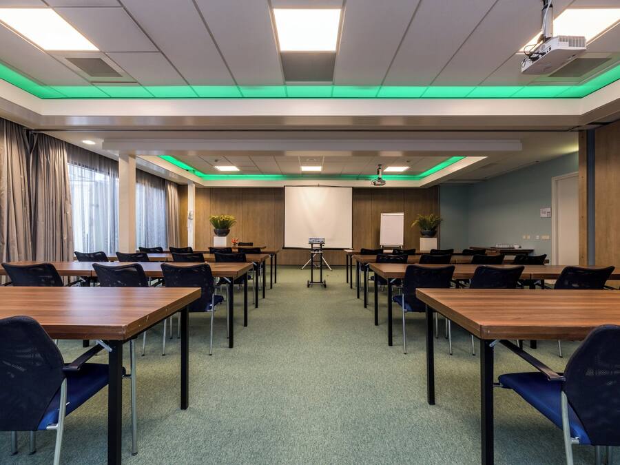 Ein Konferenzraum mit mehreren Tischen, Stühlen, einem Projektor und einer Leinwand.
