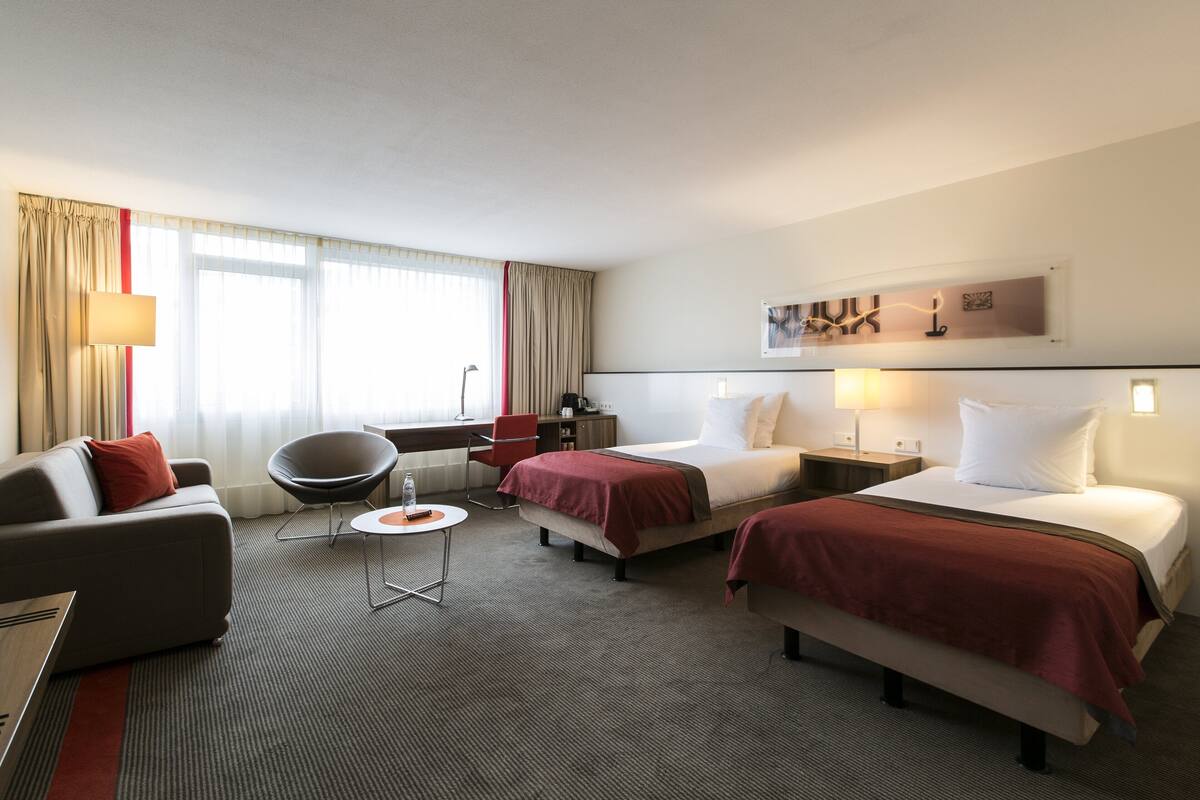 A hotel room with two beds, a sofa, a chair, a desk, and a lamp.