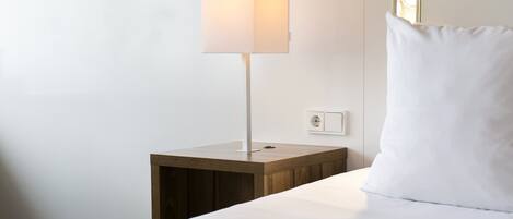A neatly made bed with a white pillow and a bedside lamp on a wooden nightstand.