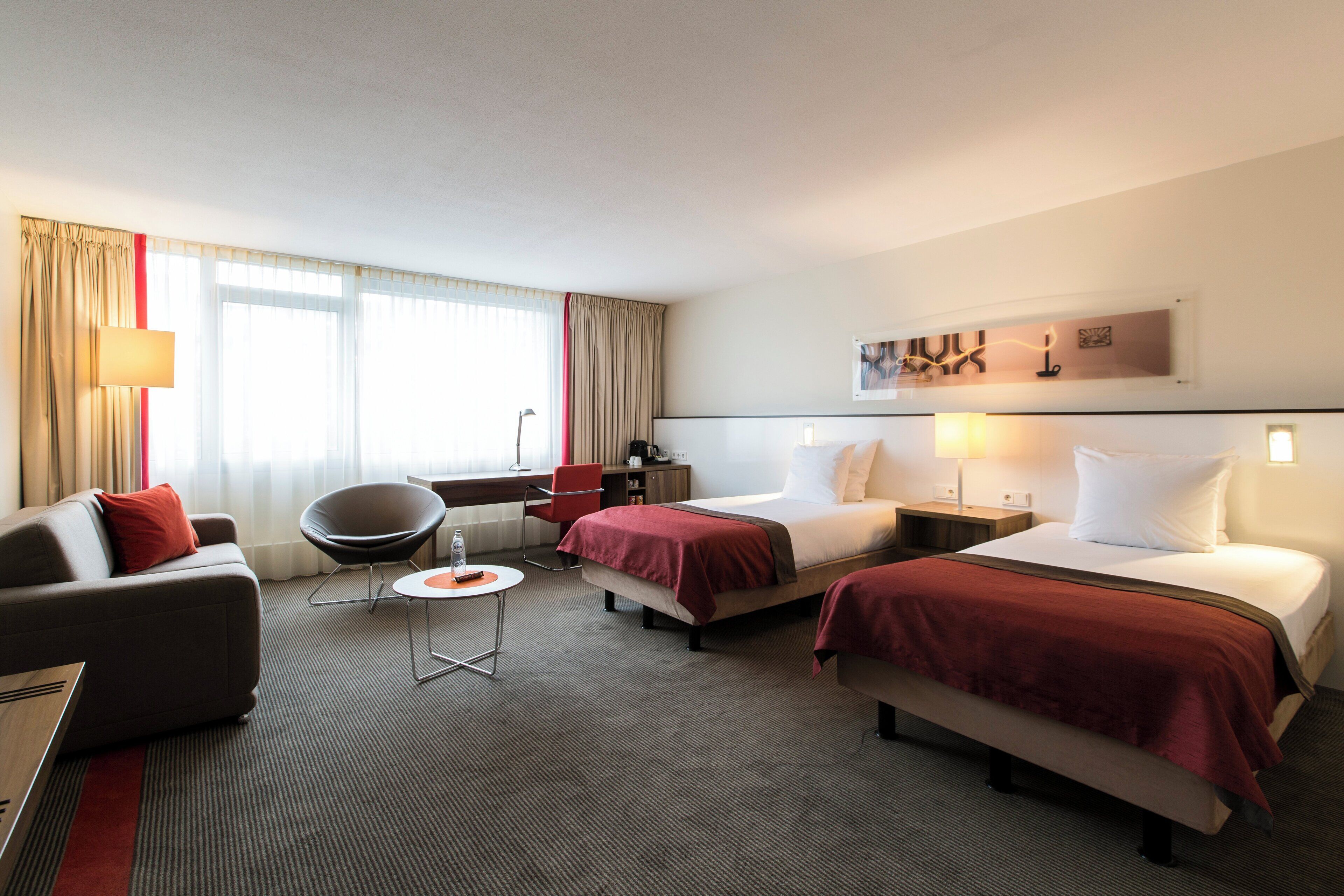 Une chambre d’hôtel avec deux lits, un canapé, une chaise, une petite table et une lampe.
