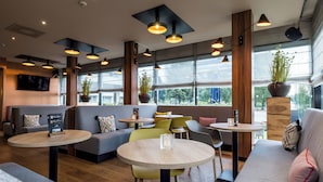 Un café moderno con mesas redondas, asientos cómodos, ventanas amplias y plantas en macetas.