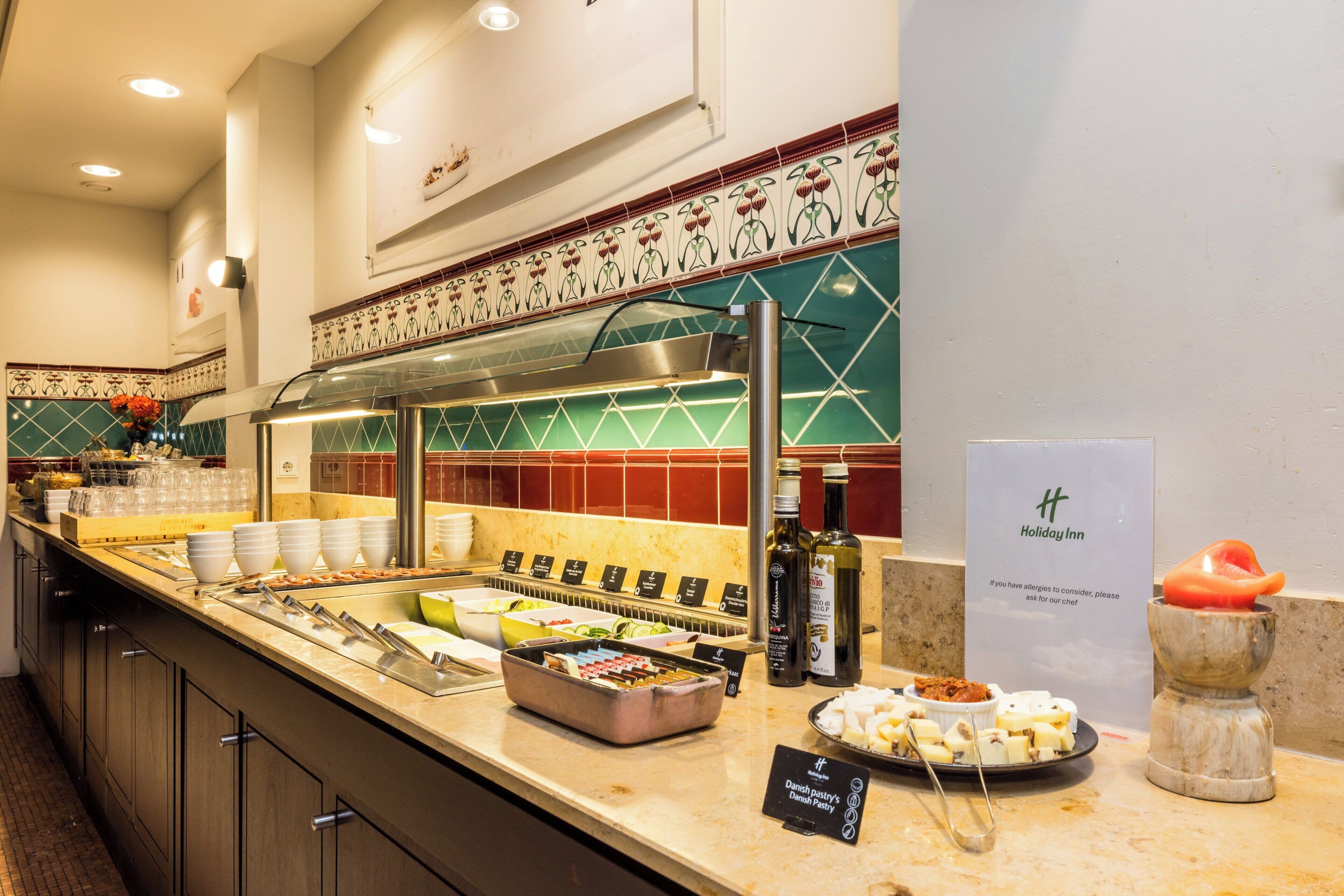 Zona de bufé con diversas opciones de comida, incluyendo una sección de pasteles daneses, y un cartel que indica la presencia de un hotel Holiday Inn.