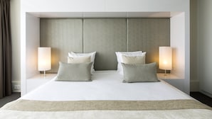 Una habitación de hotel moderna con una cama grande, dos lámparas de noche y una paleta de colores neutros.