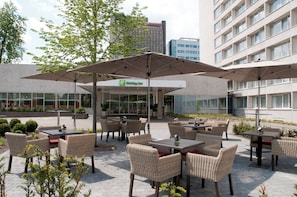 An outdoor seating area with wicker furniture and umbrellas, a Holiday Inn sign, and a building in the background.