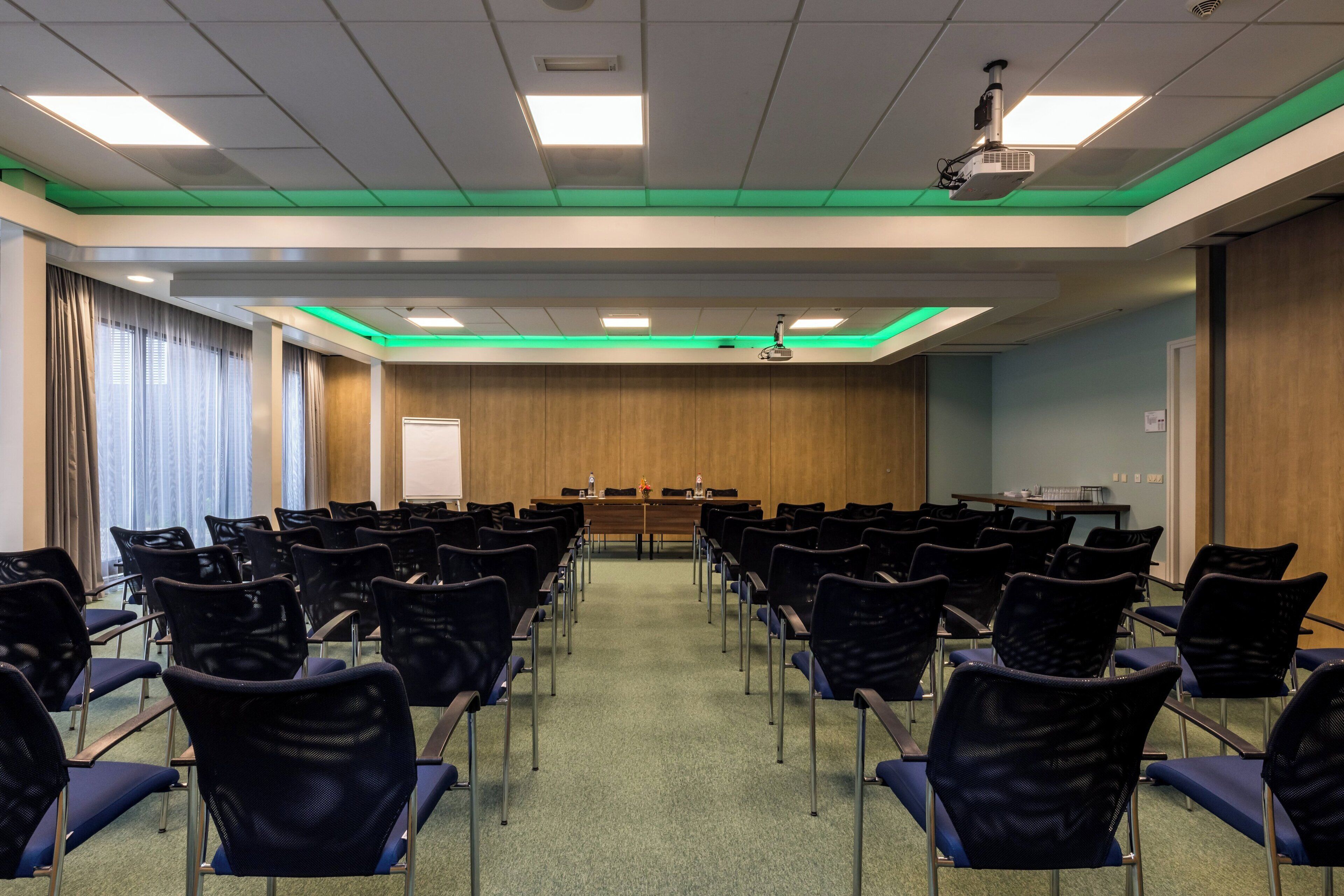 A conference room with rows of chairs, a long table, and a projector.