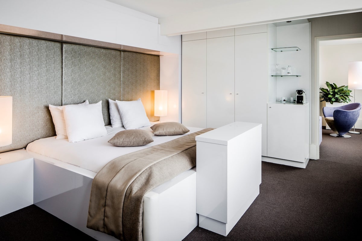 A modern hotel room with a bed, bedside tables, a desk, and a wardrobe.