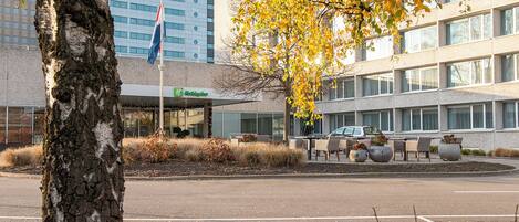 A hotel with a modern building, outdoor seating area, and a flag.