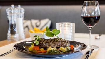 Un plato de carne con verduras y una copa de vino tinto sobre una mesa.
