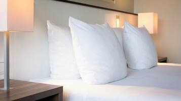 A neatly made bed with white linens and pillows, a wooden bedside table, and two wall-mounted lamps.