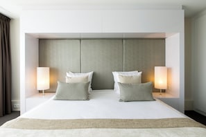 A modern hotel room with a large bed, two bedside lamps, and a neutral-toned headboard.