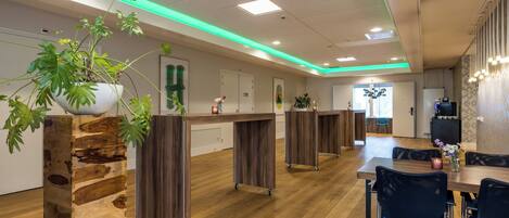 A modern hotel lobby with wooden flooring, a reception desk, and a dining area with chairs and a table.