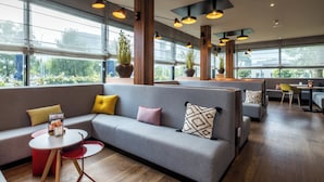 Un espacio lounge moderno con un sofá gris, cojines rojos y amarillos, y una pequeña mesa con una revista.