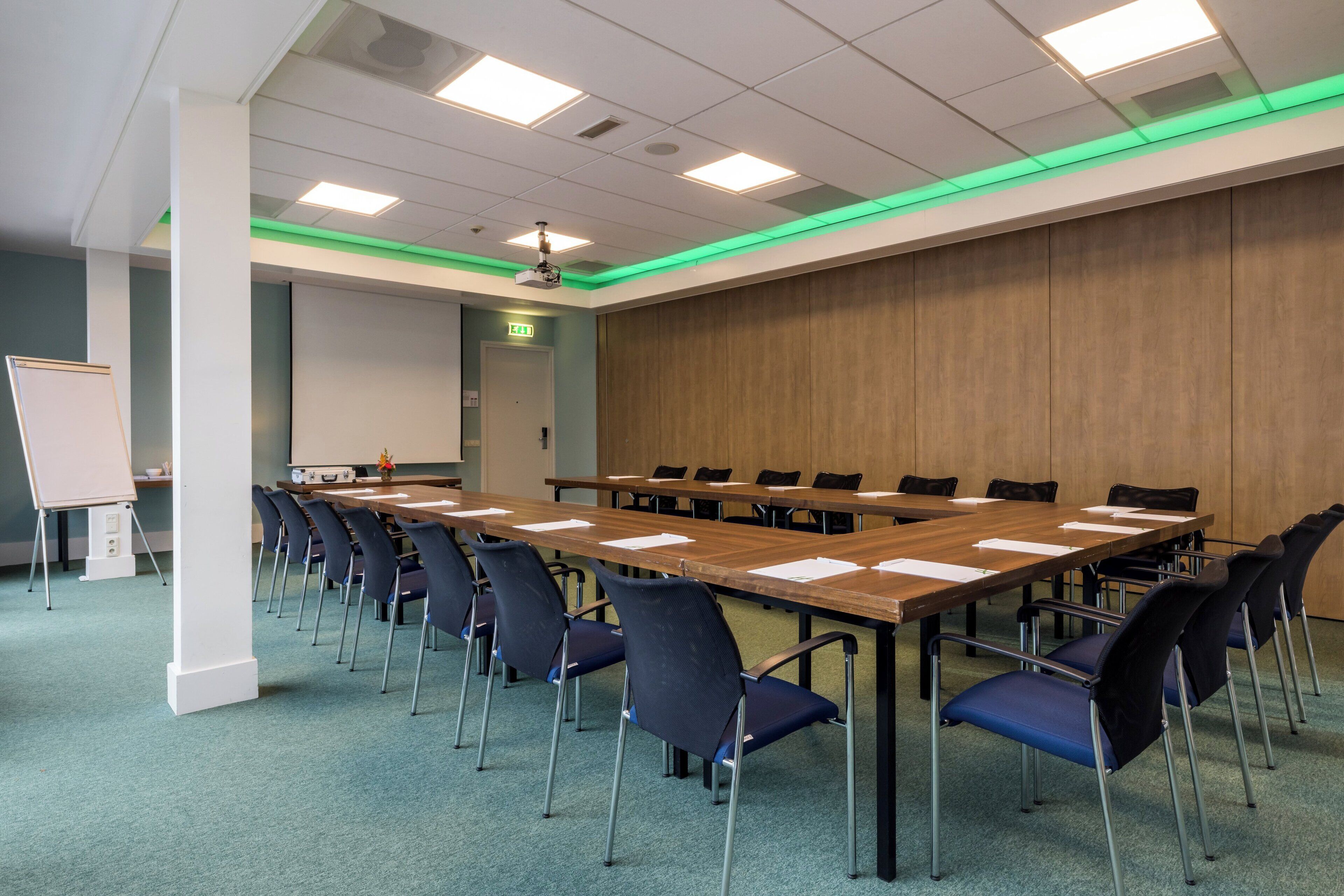 Un salón de conferencias con una larga mesa, sillas, una pizarra y un proyector.