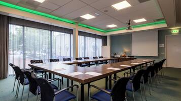 Un salón de conferencias con una larga mesa, sillas, un proyector y una pantalla.
