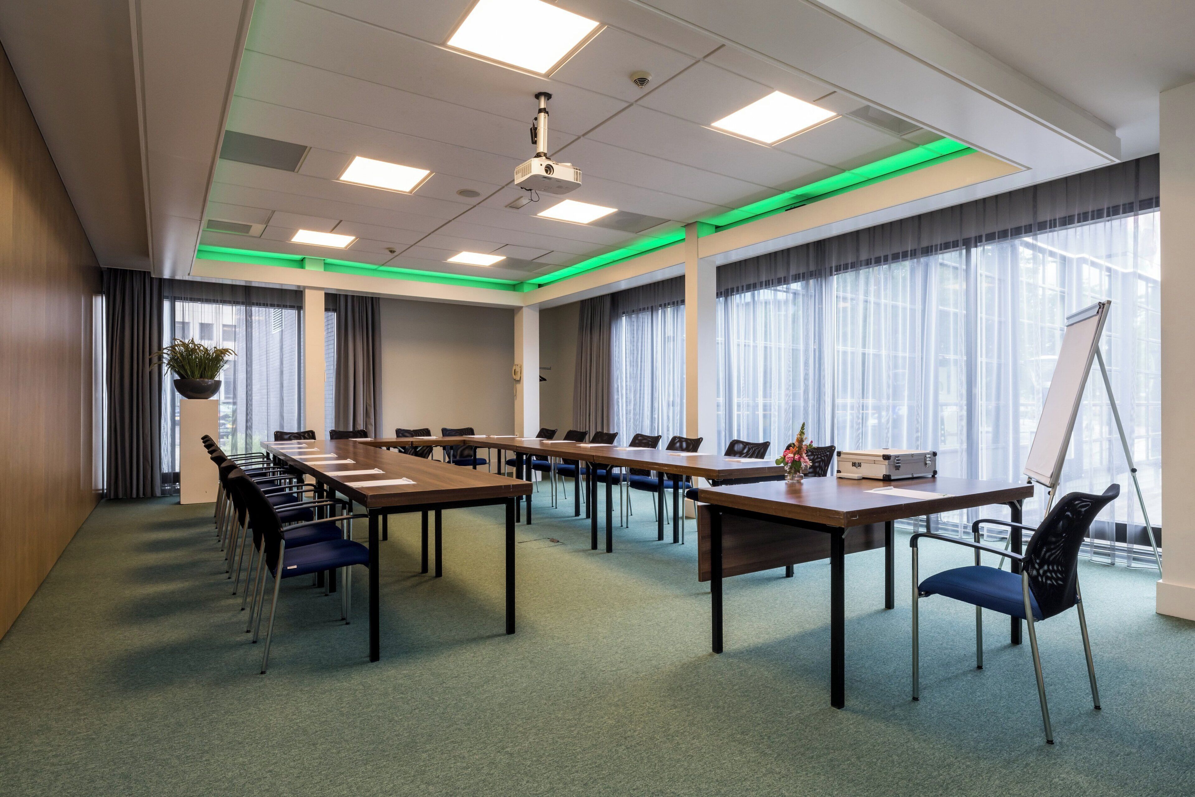 Ein Konferenzraum mit langen Tischen, Stühlen, einer Whiteboard und einem Projektor.