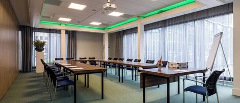 A conference room with long tables, chairs, a whiteboard, and a projector.
