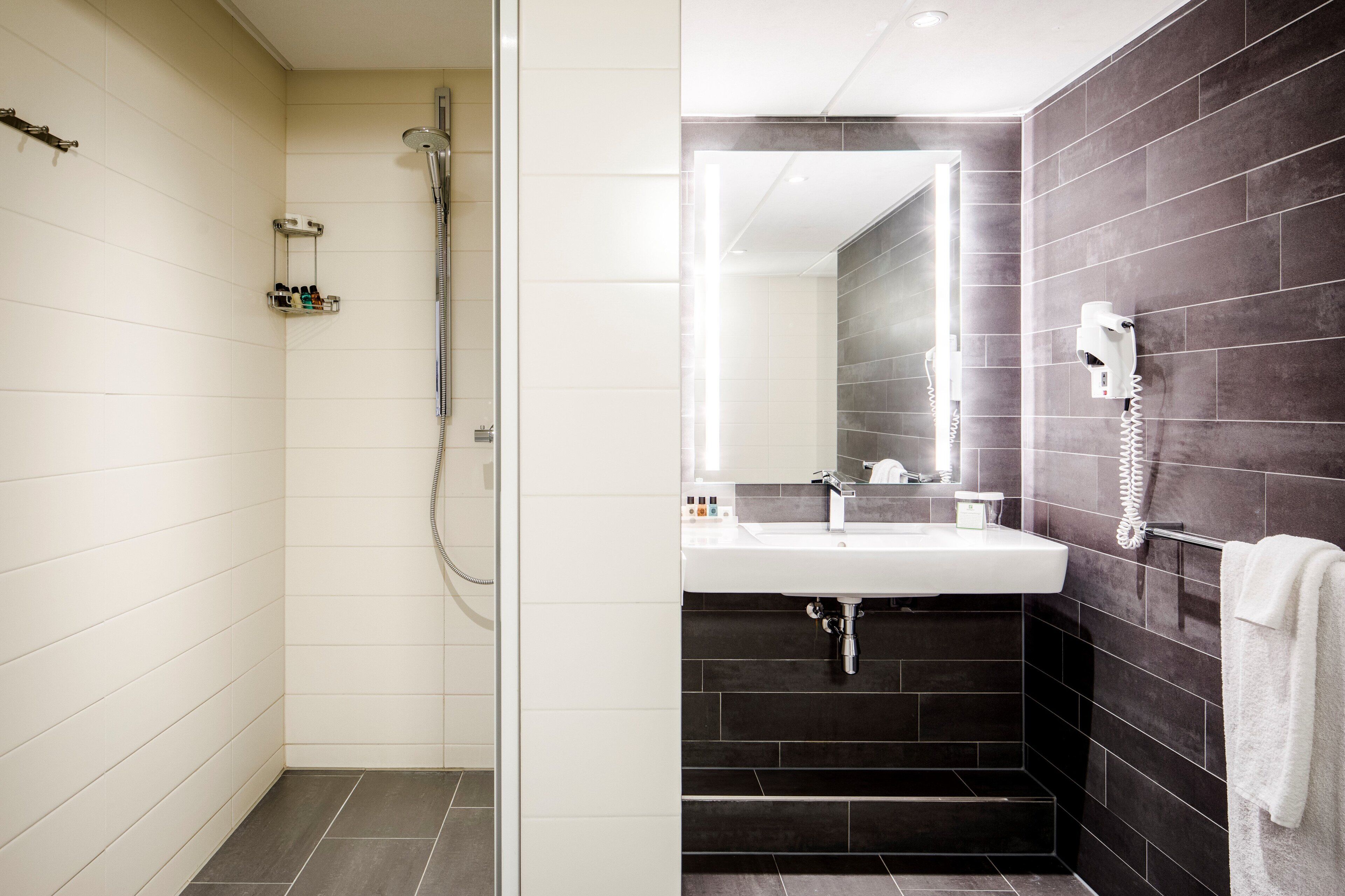 A modern bathroom with a shower, a sink, and a hairdryer mounted on the wall.
