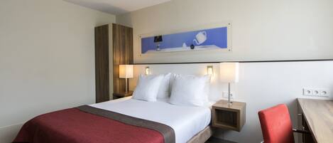 A hotel room with a large bed, two bedside tables, a red chair, and a wall-mounted artwork.