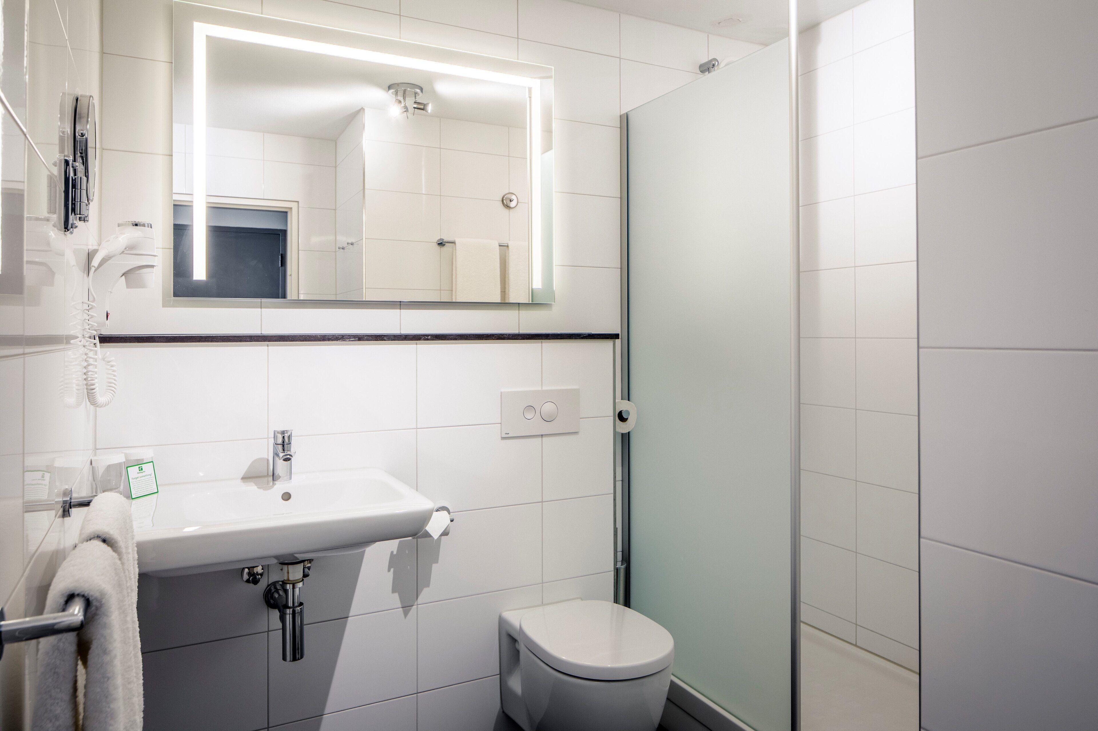 A modern bathroom with a white sink, mirror, and toilet.
