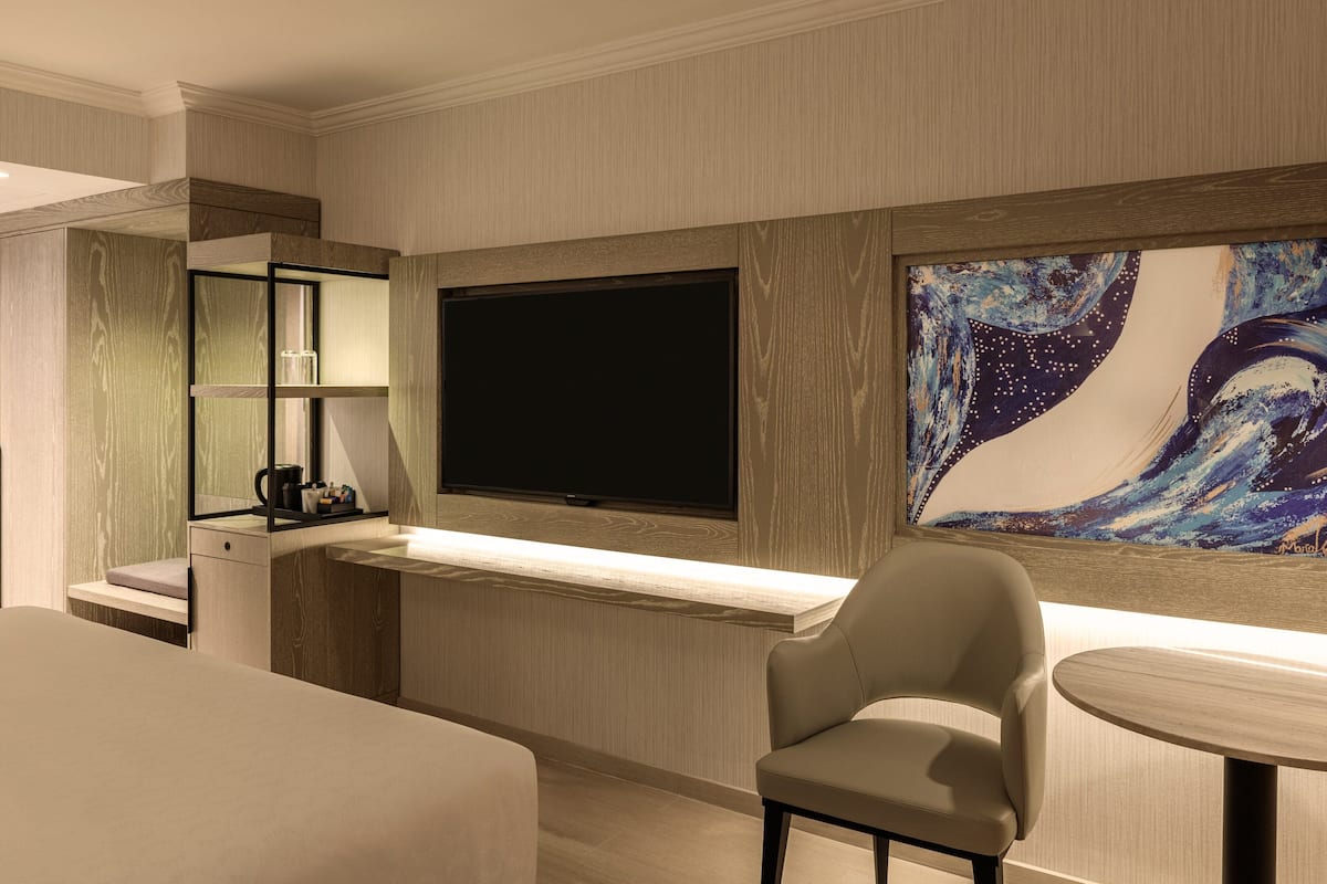 Habitación de hotel con un televisor de pantalla plana grande, un cuadro en la pared, un escritorio con una silla y una cama.