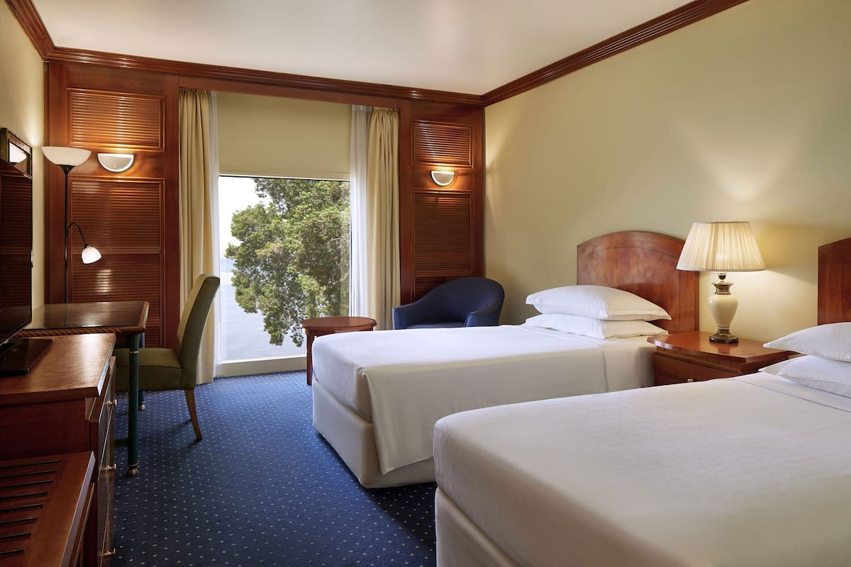 Una habitación de hotel con dos camas, un escritorio, una silla y un ventanal con cortinas.