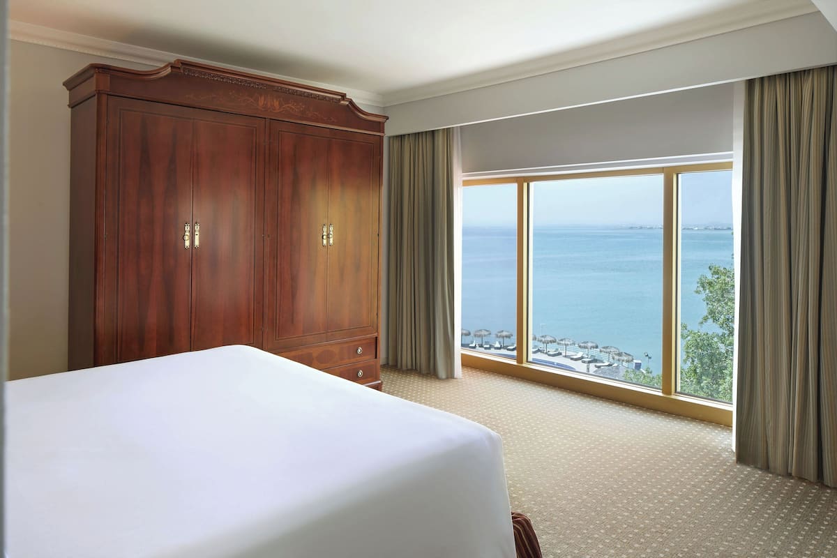 Habitación de hotel con una cama grande, un armario y vistas al mar a través de un ventanal.