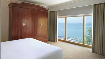 Une chambre d’hôtel avec un grand lit, une armoire et une vue sur la mer par une grande fenêtre.