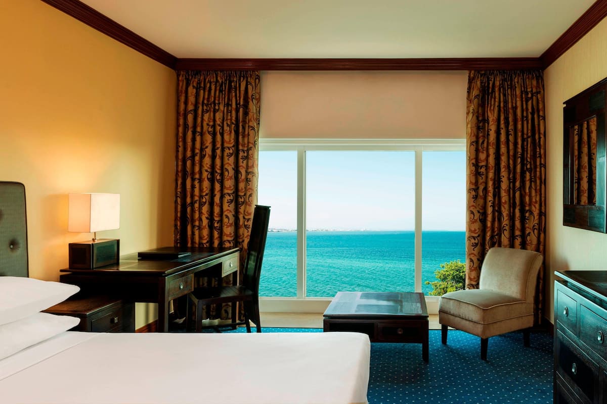 Habitación de hotel con cama, escritorio, silla y vista al océano.