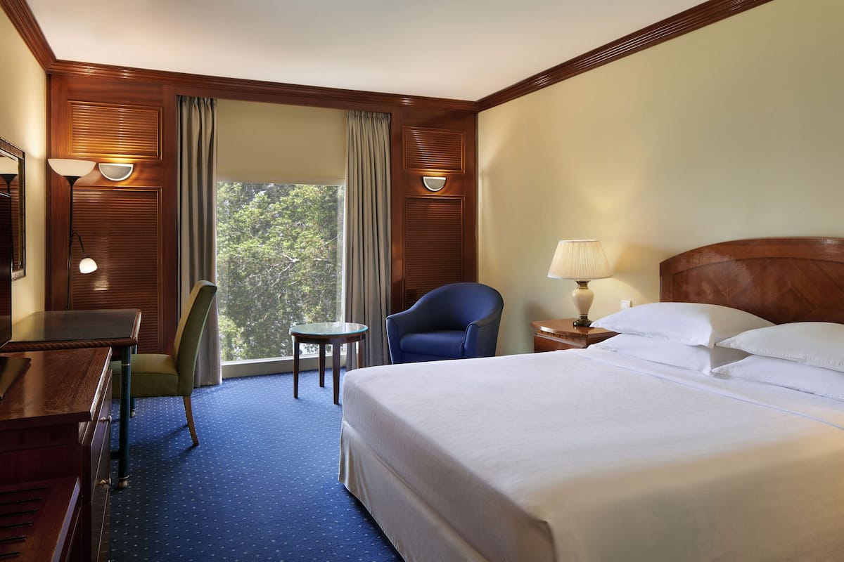 Una habitación de hotel con una cama grande, un escritorio, una silla, una mesita y una lámpara.