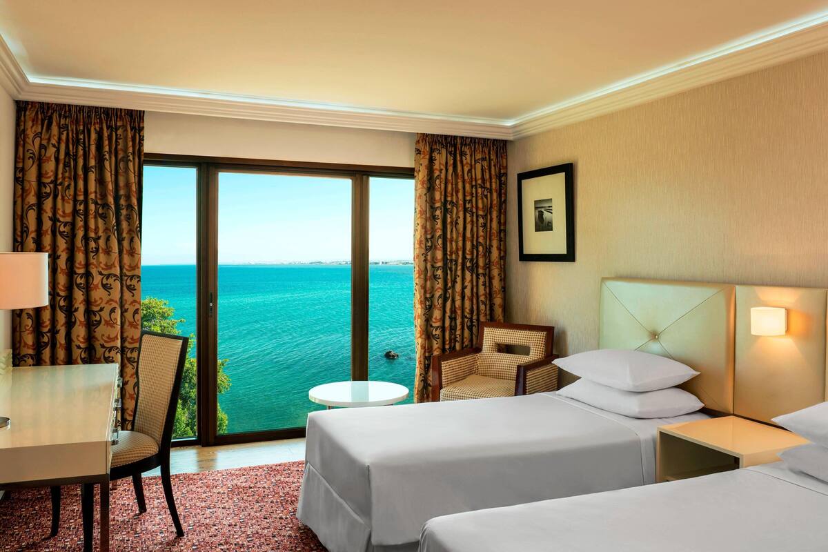 Habitación de hotel con dos camas, un escritorio, una silla y vista al mar.