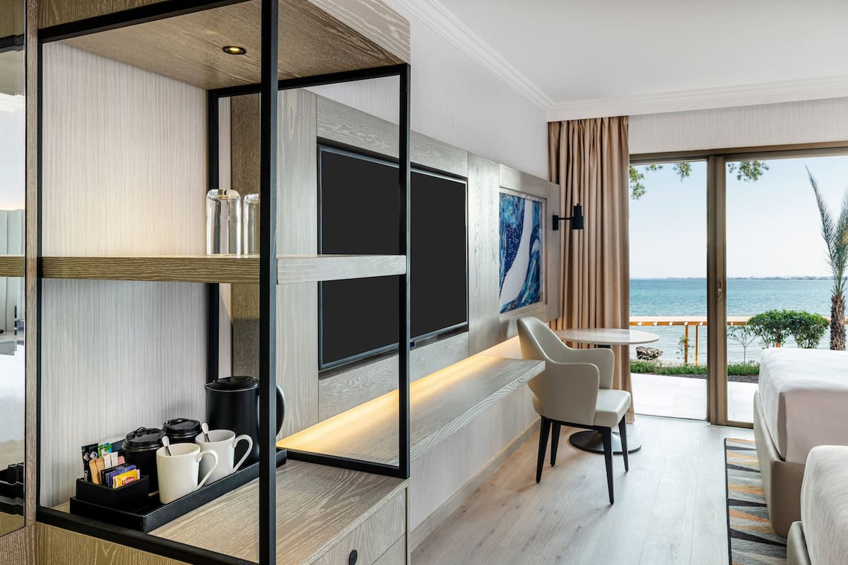 Habitación de hotel moderna con una cama grande, un escritorio con silla, una zona de café y vistas al mar.