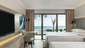 Une chambre d’hôtel dotée d’une grande télévision, d’un bureau, de deux lits et offrant une vue sur la mer.