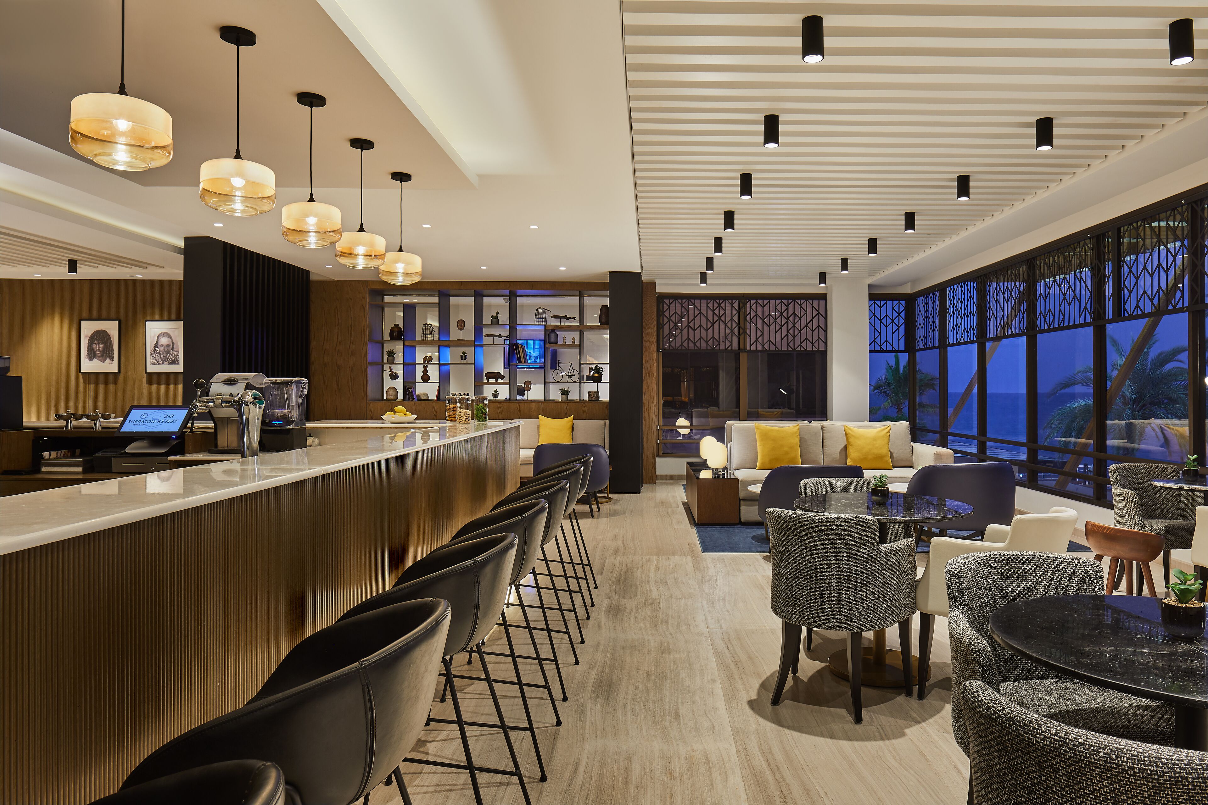 A modern hotel lobby with a bar area, seating arrangements, and large windows offering views.