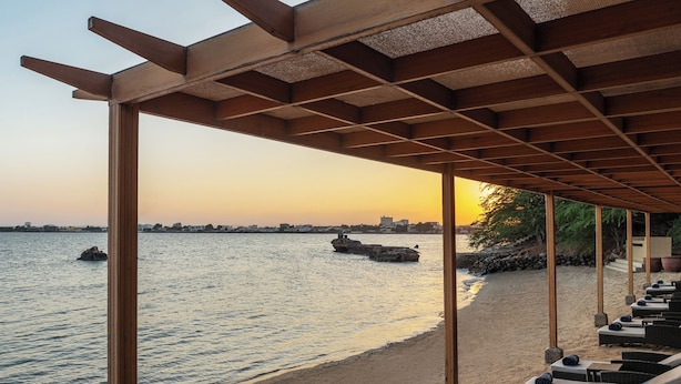Un salon de plage doté de pergolas en bois, de chaises longues et offrant une vue sur la mer.