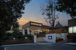 Der Eingang eines Sheraton Hotels mit modernem Design, einem überdachten Gang und einem begrünten Bereich mit Pflanzen.