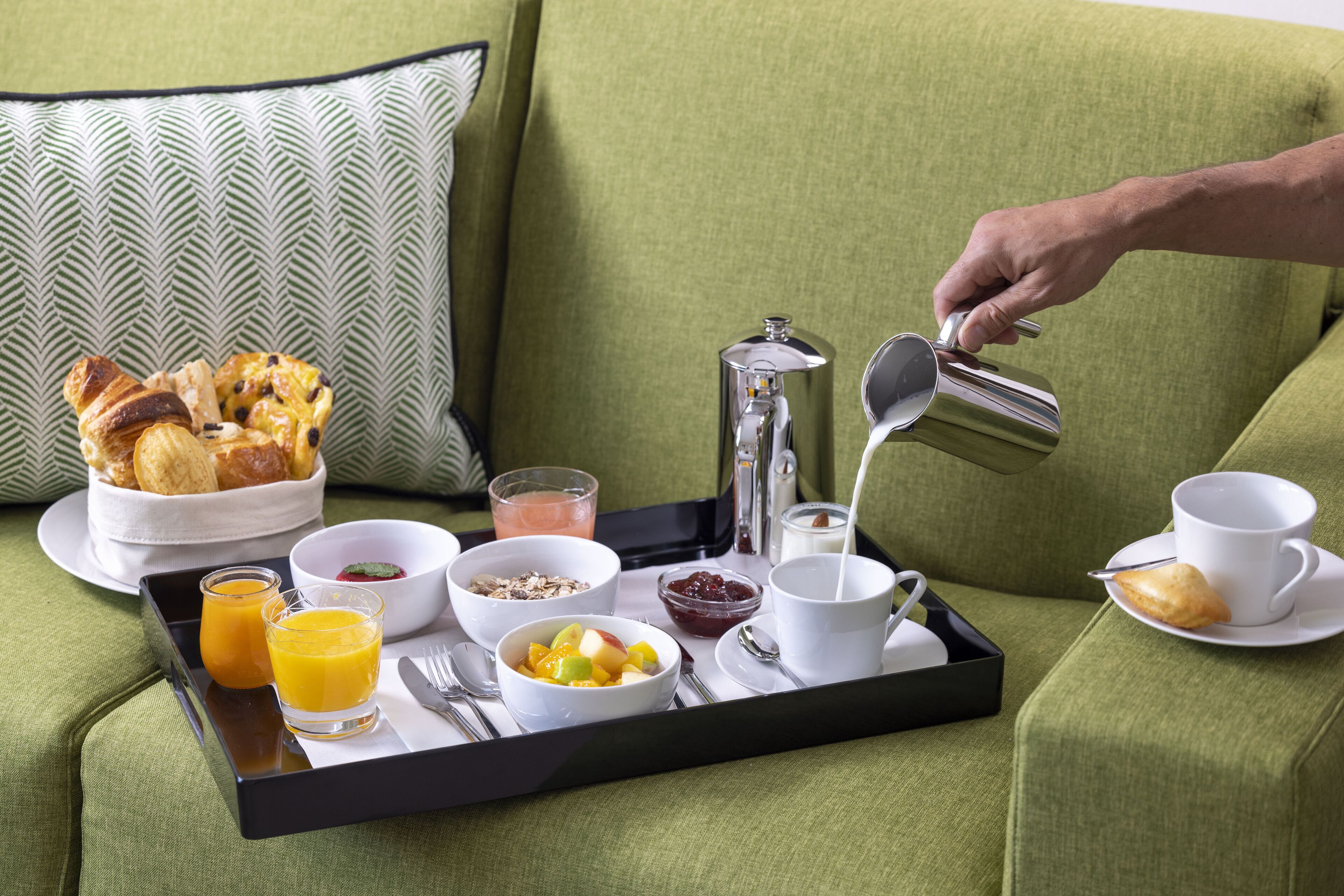 Bandeja de desayuno con diversas comidas y bebidas sobre un sofá verde.