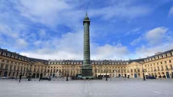 Una amplia plaza abierta con un obelisco alto en el centro, rodeada de edificios de estilo clásico y fachadas simétricas.