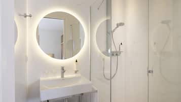 Un baño moderno con un lavamanos blanco, dos espejos redondos y una ducha con cerramiento de vidrio.