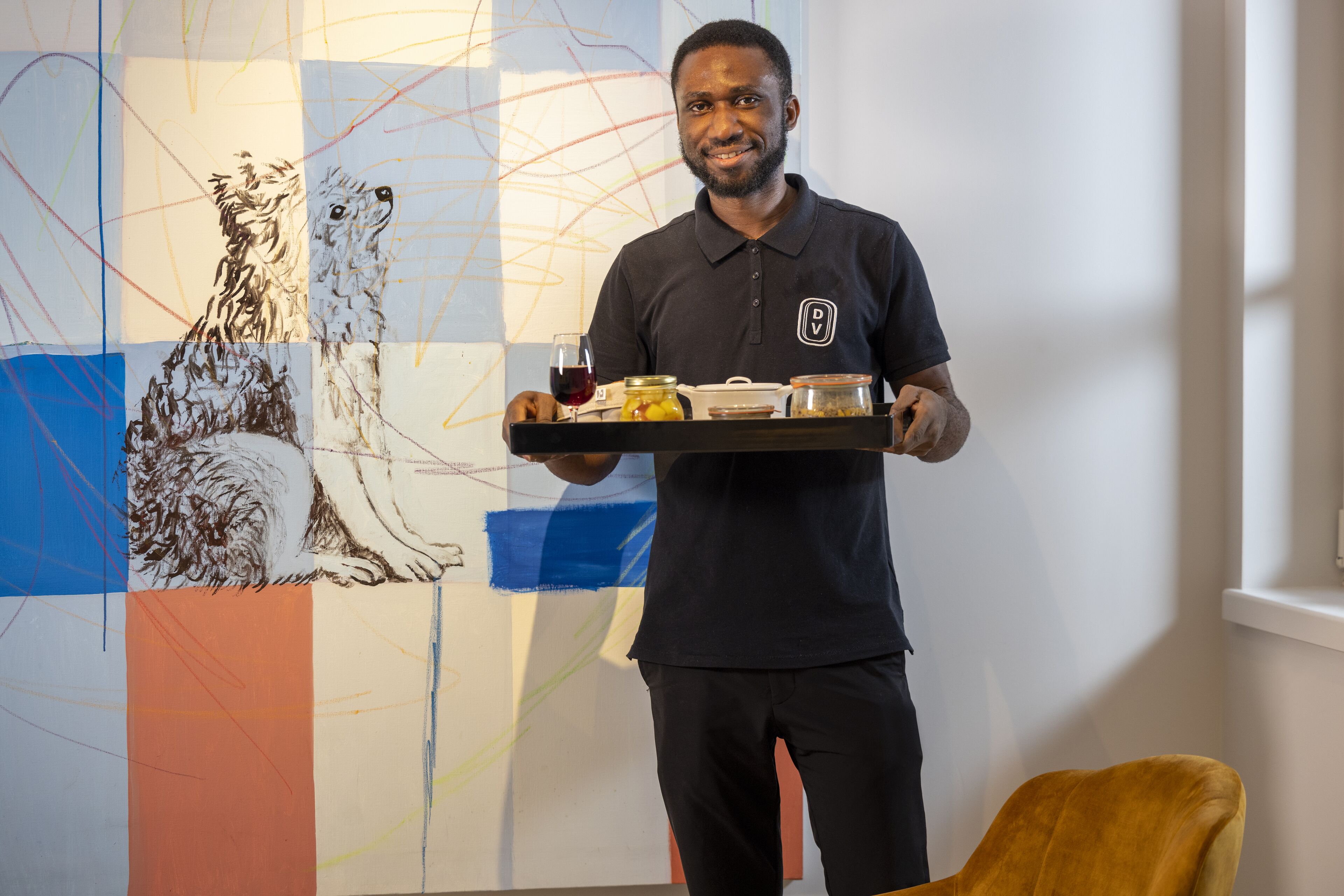Una persona sostiene una bandeja con comida y bebidas, frente a un colorido cuadro abstracto.