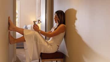 Une personne assise sur une chaise en bois dans un couloir, appuyée contre un mur, tenant un smartphone.