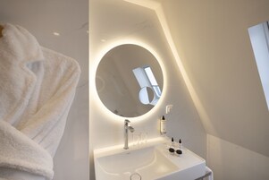 Un baño moderno con espejo redondo, lavabo blanco y un perchero para toallas.