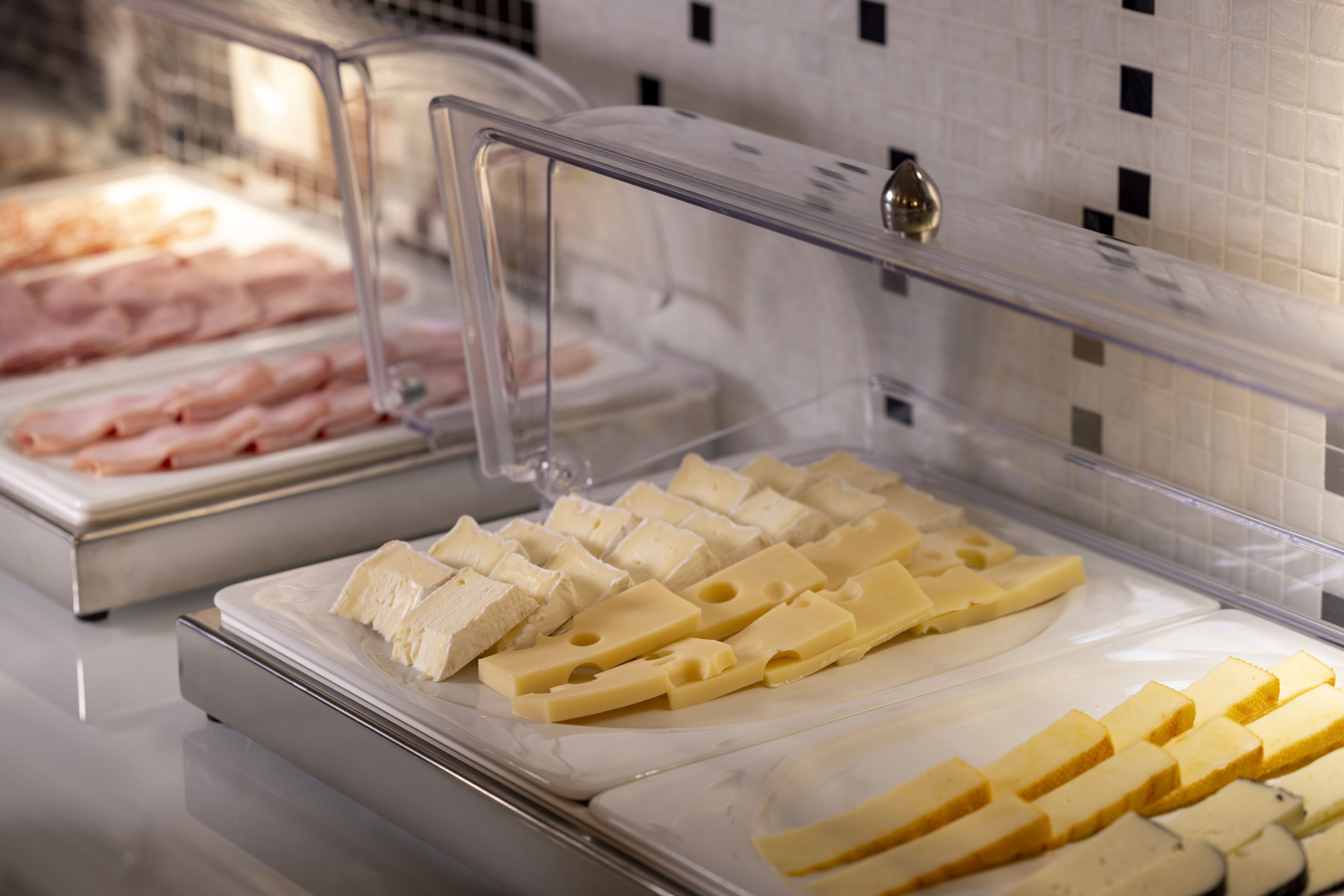 A cheese display in a deli with various types of cheese and ham.