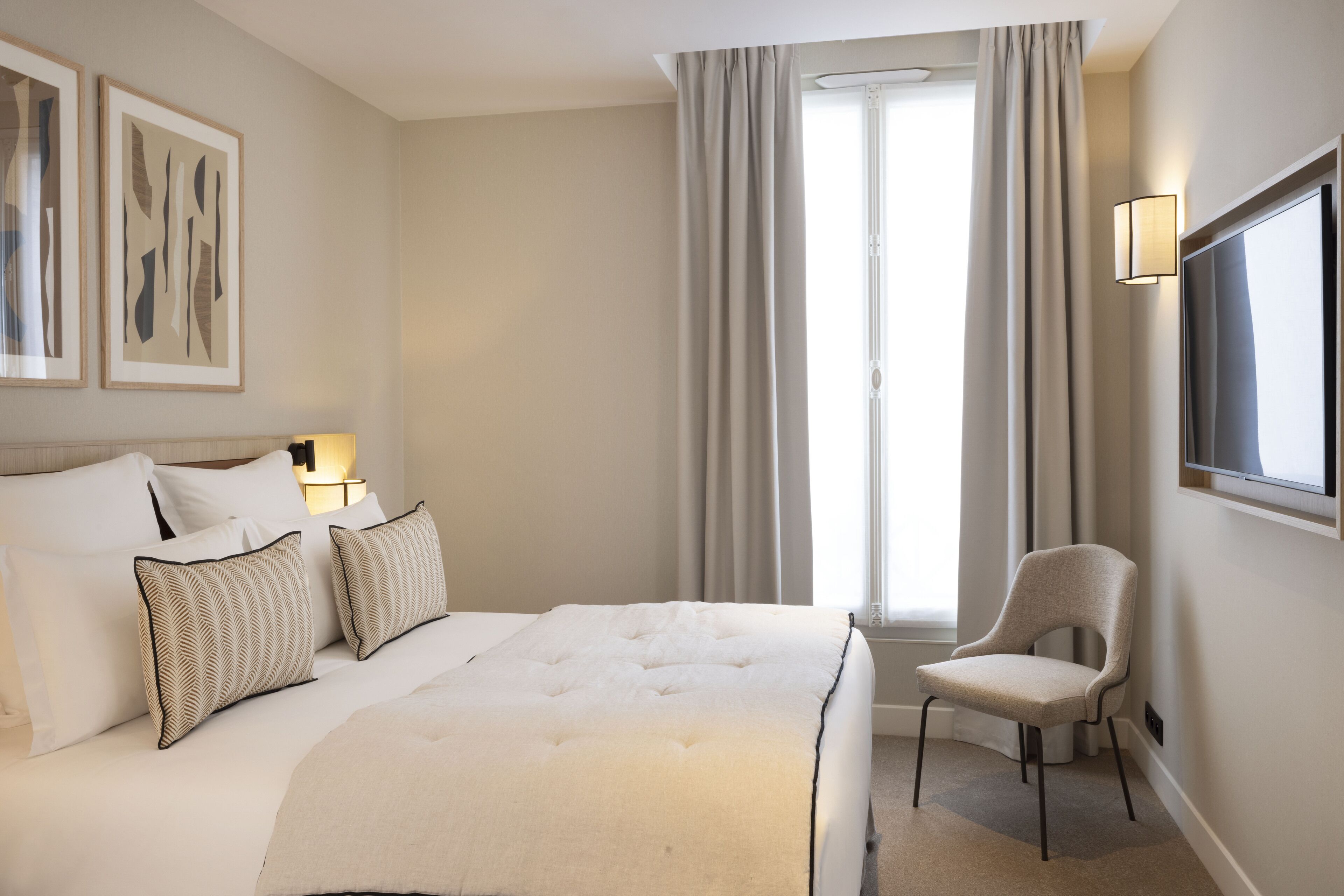 A hotel room with a large bed, a chair, a TV, and artwork on the wall.
