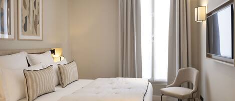 A hotel room with a large bed, a chair, a TV, and artwork on the wall.
